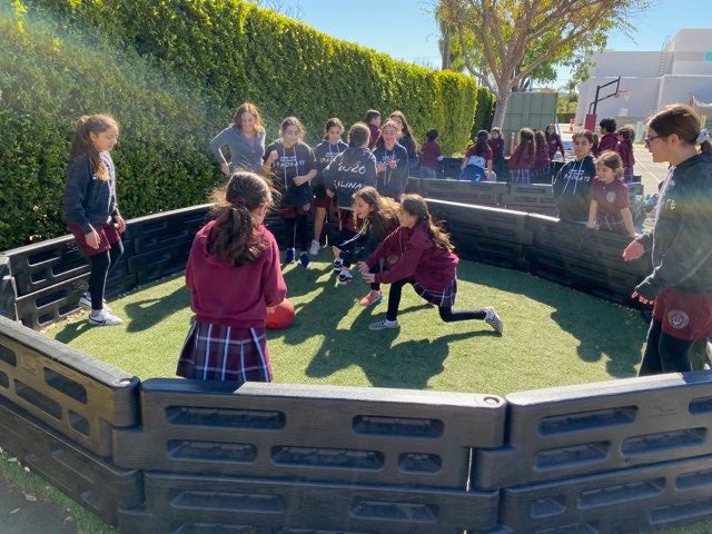 Students playing gaga ball inside a black modular gaga pit on turf at a school playground, featuring Castle Sports equipment.